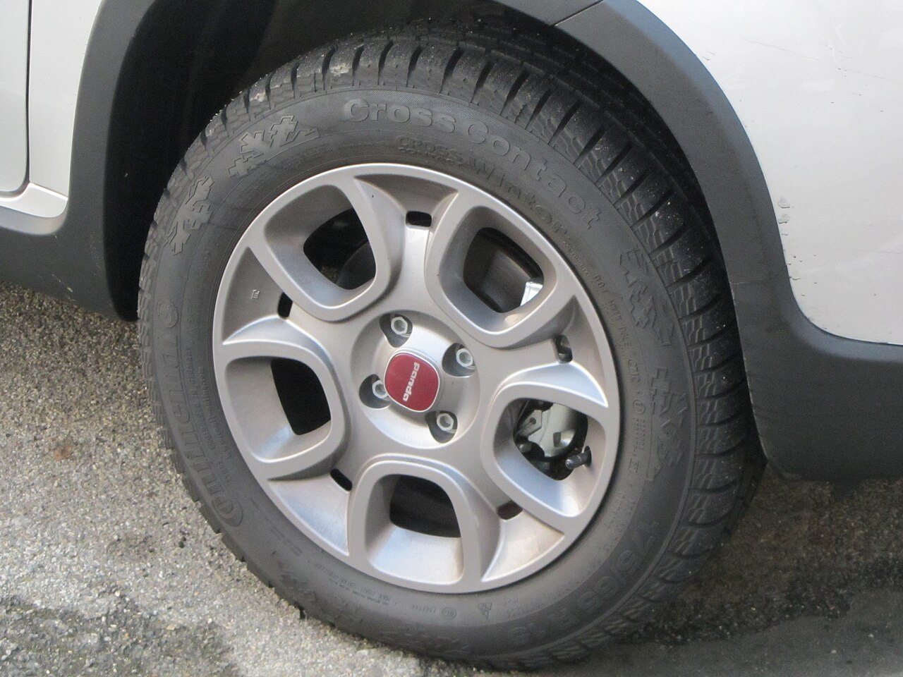 A winter tire on a grey alloy wheel of a small car, with snowflake symbols molded into the sidewall and deep, finely slit tread